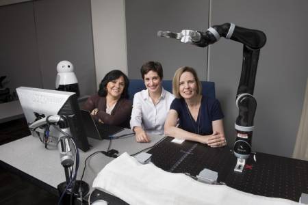 Anita Woolley, Cleotilde Gonzalez and Henny Admoni posing for a group photo in lab with robotics arm